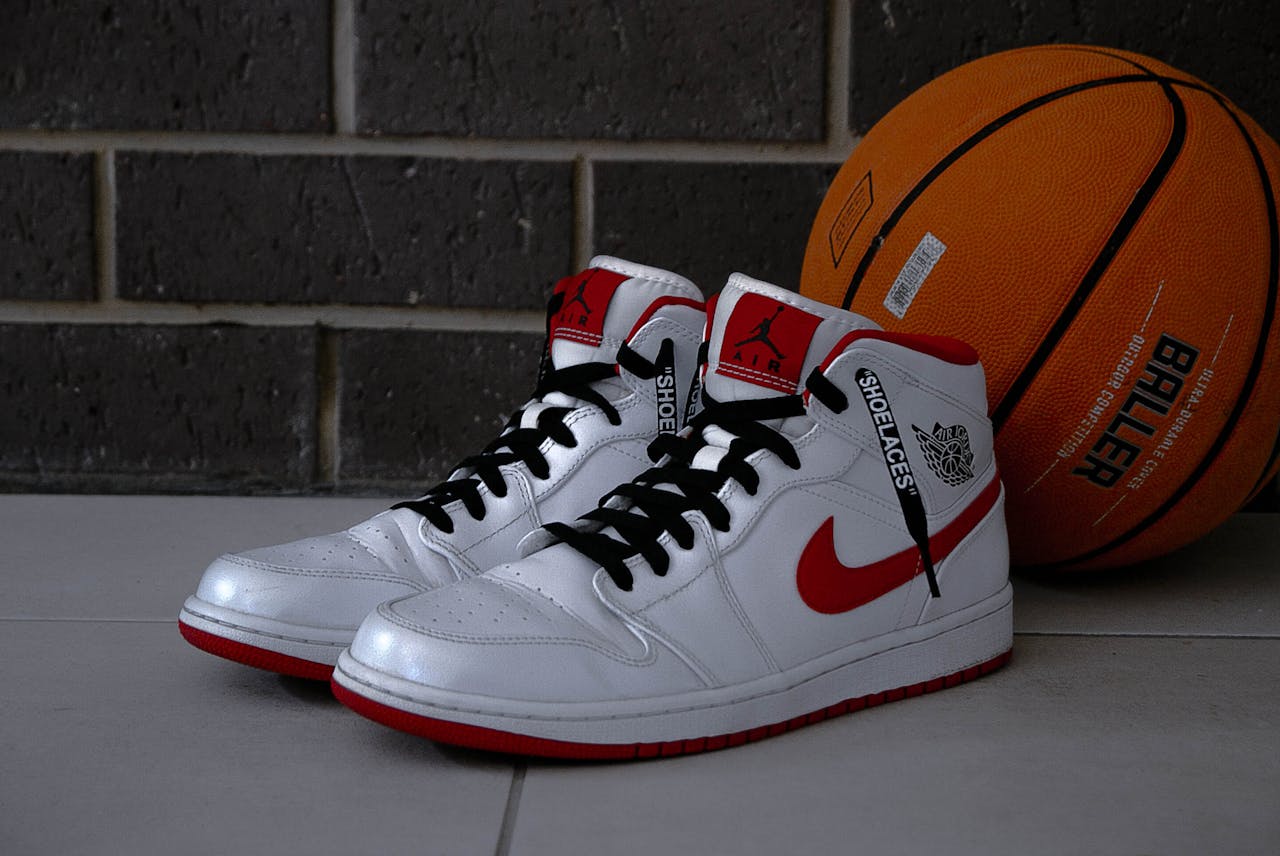 home-hero White and red basketball sneakers with an orange basketball on tiled floor.